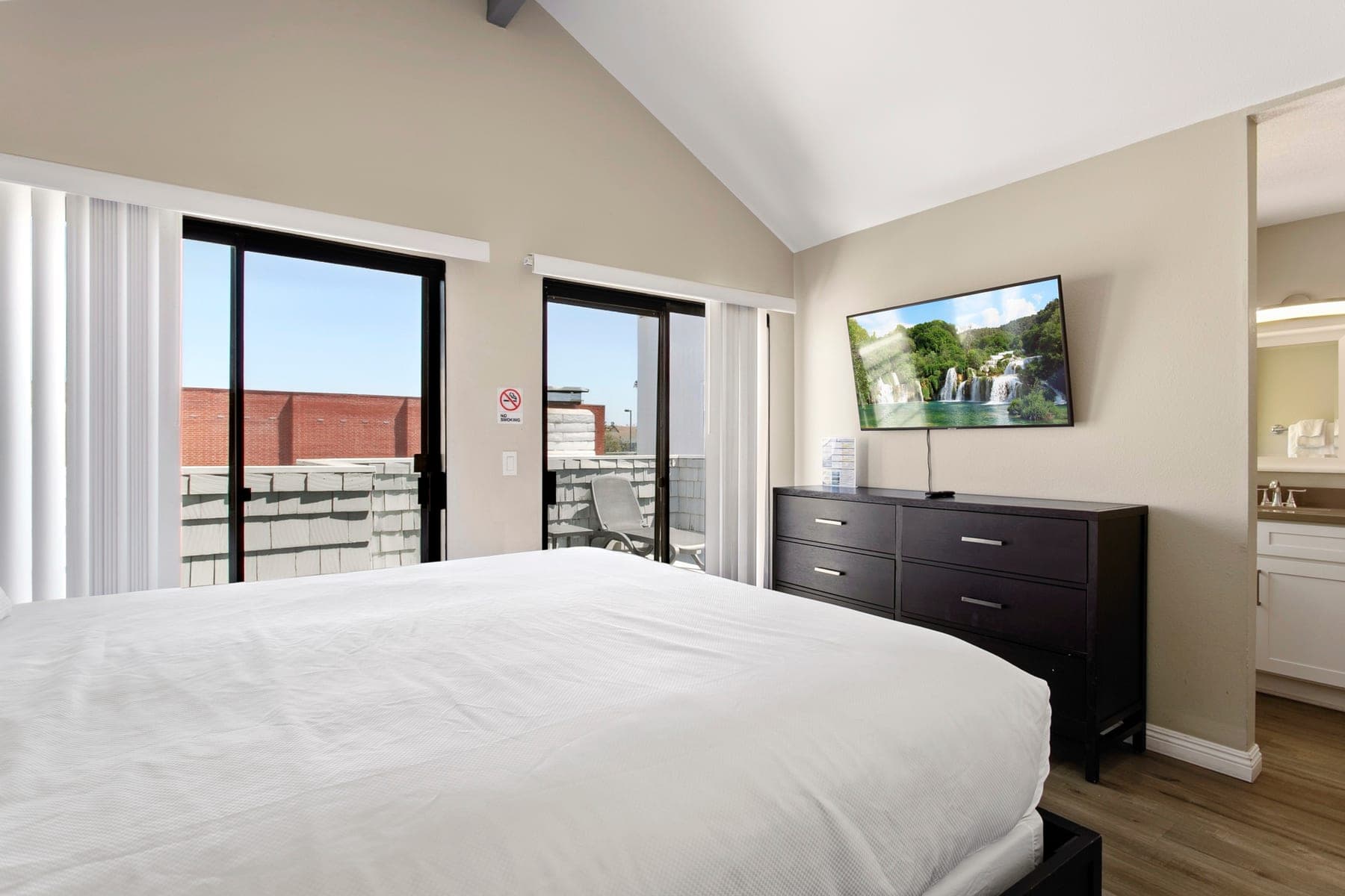 Primary bedroom with balcony doors, dresser, and Smart TV