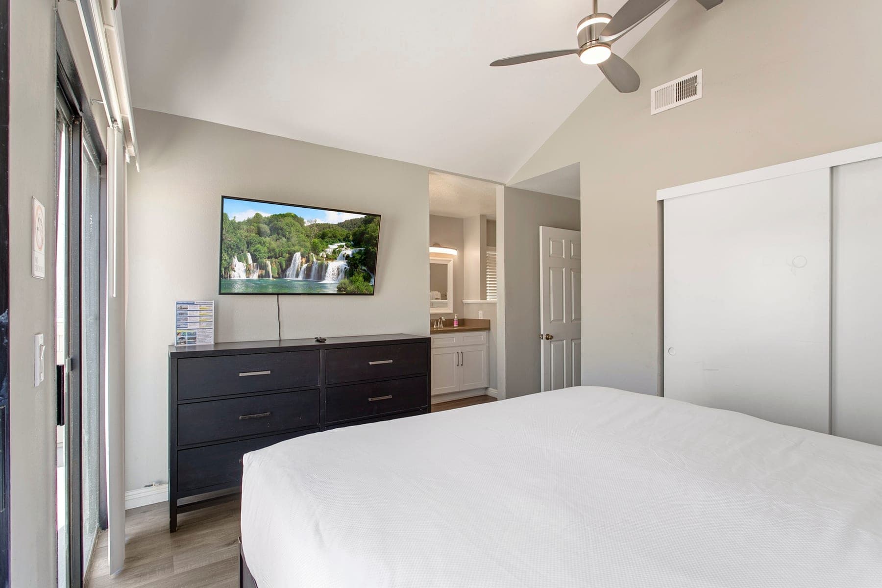 Primary bedroom with wall-mounted Smart TV, dresser, and closet