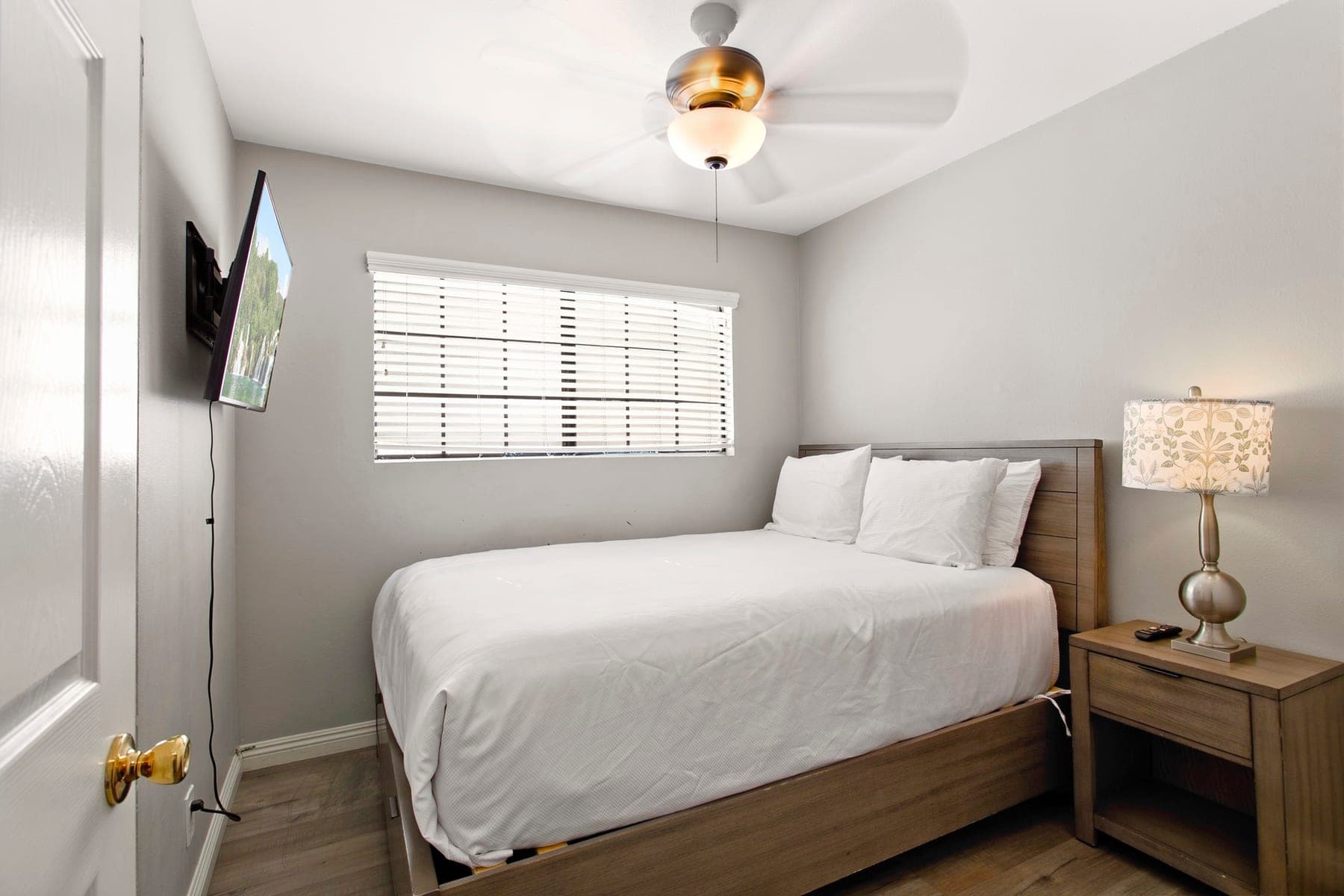 Queen bedroom with window, bedside lamp, and wall-mounted TV